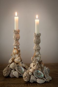 two candles that are sitting next to each other on a wooden table with shells and seashells