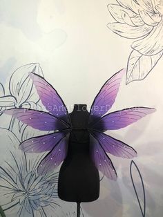 a purple and black butterfly wings on a mannequin's head with flowers in the background