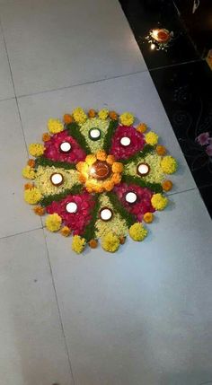 an arrangement of flowers and lit candles on the ground in front of a person's feet