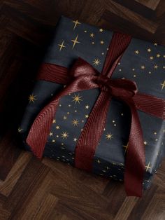 a gift wrapped in blue and gold stars with a red ribbon on it sitting on a wooden floor