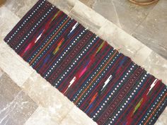 a multicolored striped rug on the floor next to a potted plant in a room