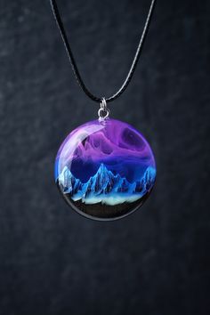 Handmade round Northern lights pendant from black hornbeam wood and epoxy resin with snow mountains inside.  Glow in the dark! D E T A I L S : * Made to order epoxy resin necklace * Materials: black hornbeam wood (impregnated with protective eco oils) and epoxy resin * Available in three sizes: 34mm, 31mm, 28mm. * Shipped in a box for easy gift giving * Each piece is handmade. The wood we use is of high quality and absolutely smooth to the touch. The resin is polished to a mirror finish. N E C K Mystical Resin Necklaces For Gifts, Epoxy Resin Necklace, Multicolor Resin Pendant Jewelry, Resin Pendant Diy, Nature-inspired Resin Round Pendant Jewelry, Blue Spiritual Resin Necklaces, Resin Galaxy Pendant, Snow Mountains, Stainless Steel Fittings