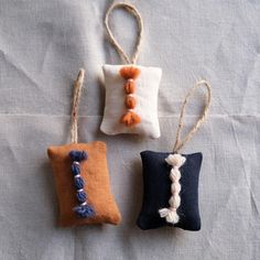 three small pillows with tassels hanging from them on a white cloth covered surface