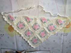 a crocheted pink and white flowered triangle hanging from the side of a wall