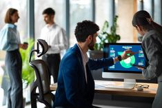 two people are looking at a computer screen while others stand in the background and look on