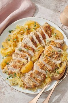 a white plate topped with meat and potatoes next to a wooden spoon on a table