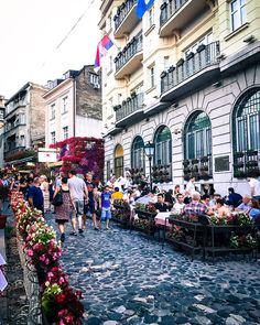 many people are walking down the street in front of some buildings with flowers on them