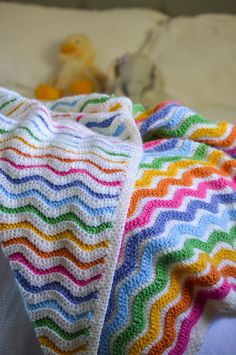 a crocheted blanket laying on top of a bed next to a stuffed animal