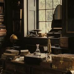 an old fashioned desk in front of a window filled with books and other items on it