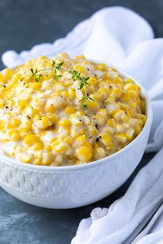 a white bowl filled with corn on top of a blue table cloth next to a fork