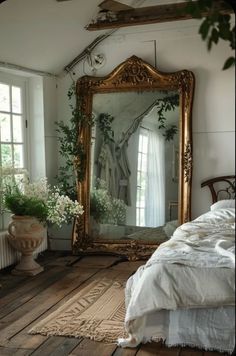 a large gold framed mirror sitting on top of a wooden floor next to a bed