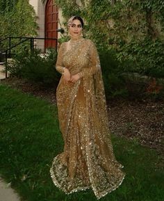 a woman standing in front of a house wearing a gold gown and headpieces