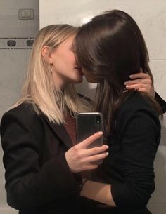 two women are kissing each other in front of a mirror and one is holding a cell phone