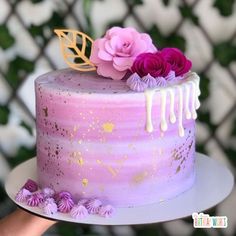 a pink cake with white icing and purple flowers on top is being held by a person