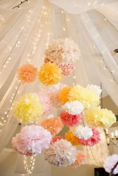 paper pom poms hanging from the ceiling in a room with string lights and white curtains