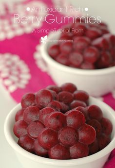 two white bowls filled with raspberries sitting on top of a pink table cloth