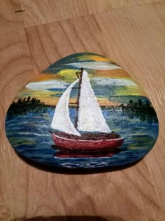 a painted rock sitting on top of a wooden table next to a painting of a sailboat