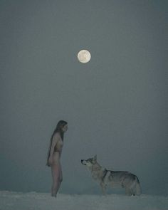 a woman standing next to a dog on top of a snow covered field under a full moon