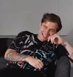 a man sitting on top of a black couch next to a white wall and smiling