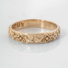 a gold wedding ring with an ornate design on it's side and the word happily written in cursive writing