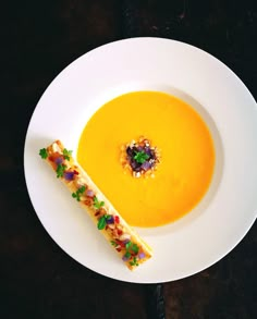 a white plate topped with a yellow soup next to a piece of bread