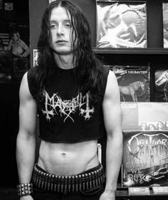 a man with long hair and no shirt standing in front of some recordshelves