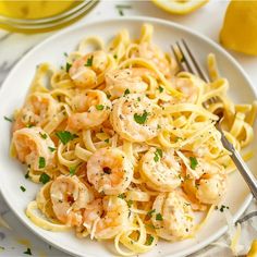 a white plate topped with pasta covered in shrimp and parsley next to lemon wedges