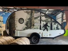 a man is walking through the woods in front of an oval shaped trailer with trees on it