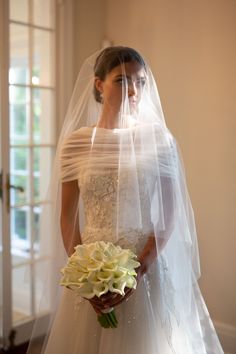 a woman in a wedding dress and veil holding a flower bouquet with her hands behind her back