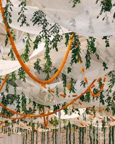 an orange and white wedding decoration with greenery hanging from it's ceiling,