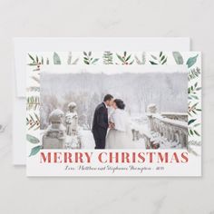 a merry christmas card with a couple kissing in front of snow covered trees and greenery