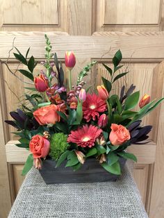 an arrangement of flowers in a wooden box on a table next to a wood door