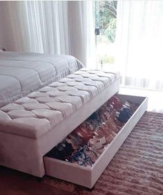 a white bed with drawers underneath it in a room next to a window and curtains