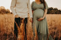 a pregnant couple holding hands while standing in tall grass