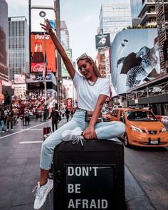 a woman sitting on top of a box in the middle of a street with her arms up