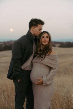 a pregnant couple standing in a field at sunset