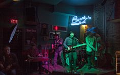 a group of people playing instruments in a dark room with neon signs on the wall