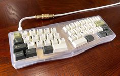 a computer keyboard sitting on top of a wooden table next to a charger and plugged in