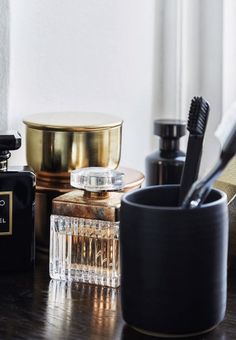 an assortment of personal care items sitting on a table next to a cup and brush