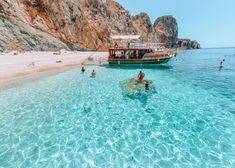 people are swimming in the clear blue water next to a rocky beach with a boat