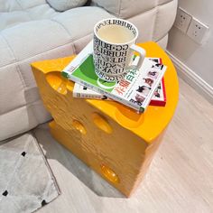 a cup of coffee sitting on top of a cheese shaped table next to a couch