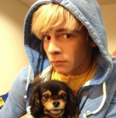 a boy in a blue hoodie holding a small black and white dog with blonde hair