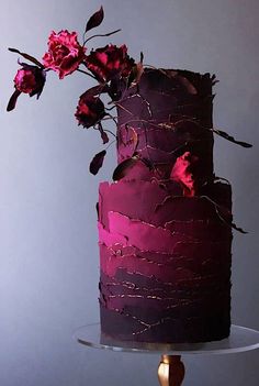 a three tiered purple cake with pink flowers on top