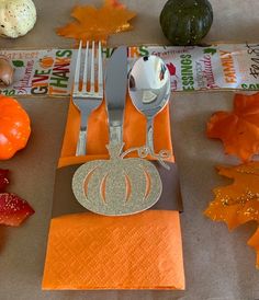 a place setting with silverware and orange napkins on top of an orange table runner