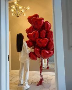 a woman is holding red balloons in the shape of hearts