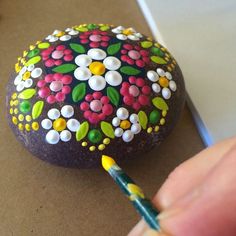 a painted rock with flowers on it and a person holding a pencil in their hand