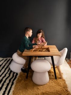 two children sitting at a table playing with a board game on top of a rug