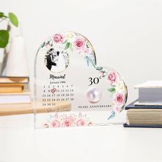 a heart shaped desk calendar with flowers on it and a book next to it in front of a stack of books