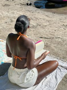 a woman sitting on the beach reading a book