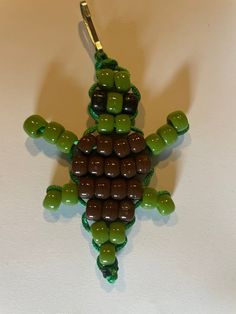 a green and brown beaded turtle ornament hanging from a hook on a white wall